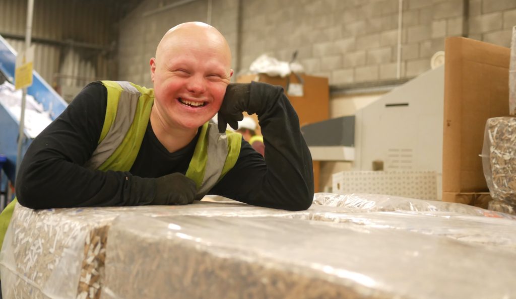 A smiling young man rests on bales of carboard.